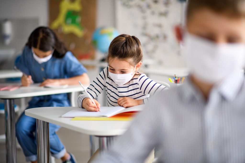 Niños pequeños con mascarilla en la escuela después de la cuarentena y encierro del covid-19, escribiendo.